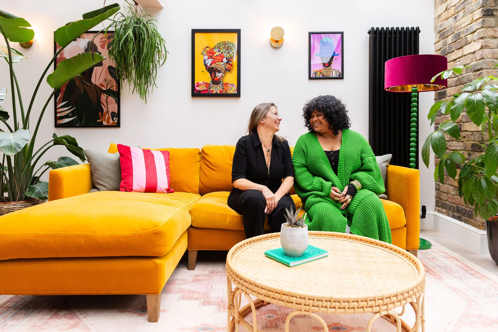 Two people sitting on a yellow sofa in a colourful living room.